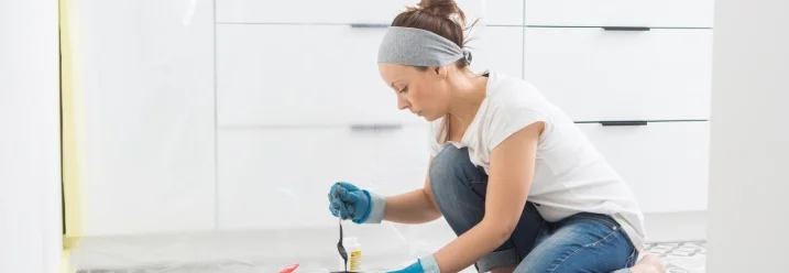 Person rührt schwarze Farbe in einer Farbdose mit einem Holzstab an.